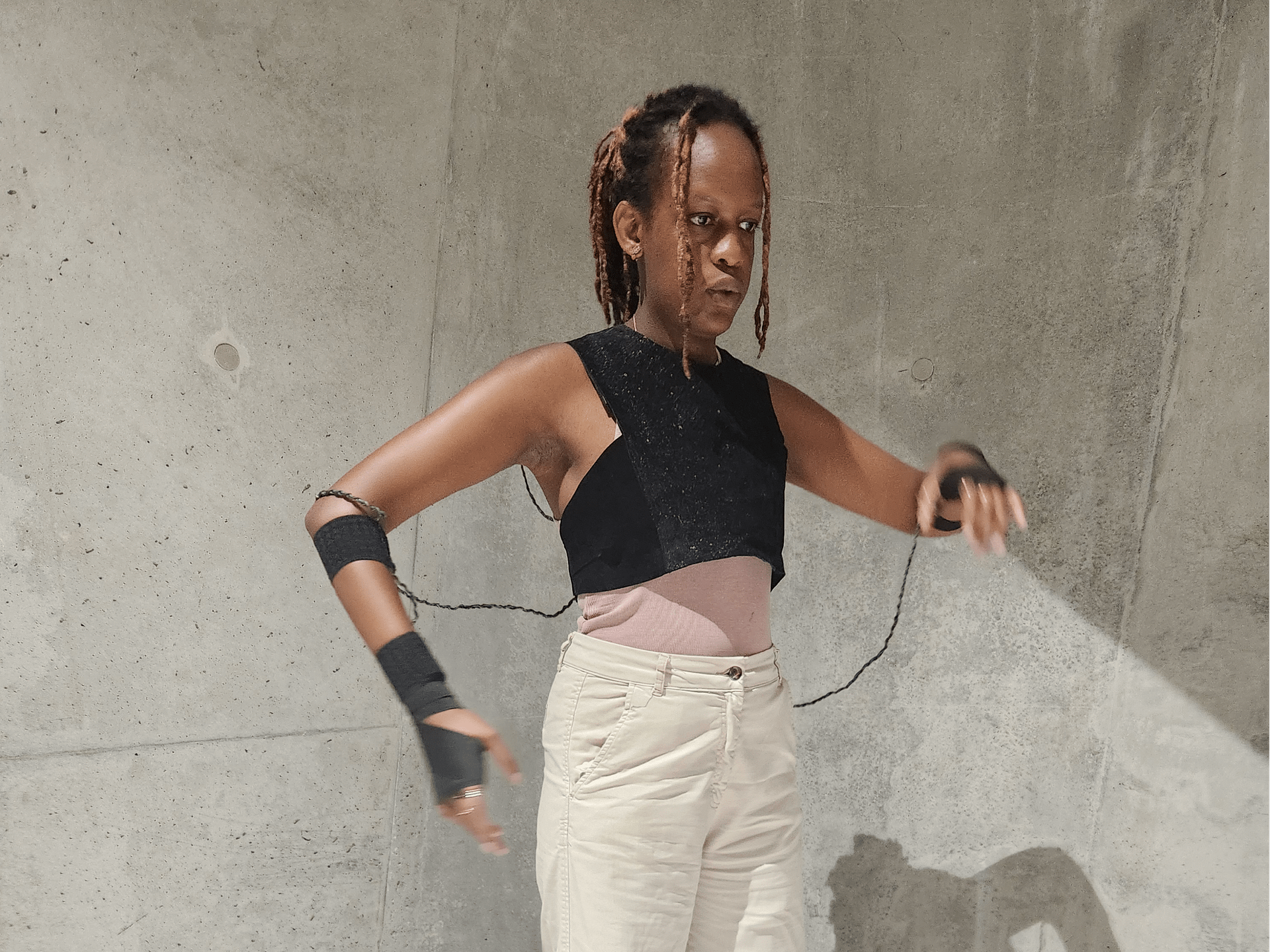 Nyokabi Kariuki wearing a percussion instrument. The instrument is a leather chest piece and leather gloves, connected by braided cables.
